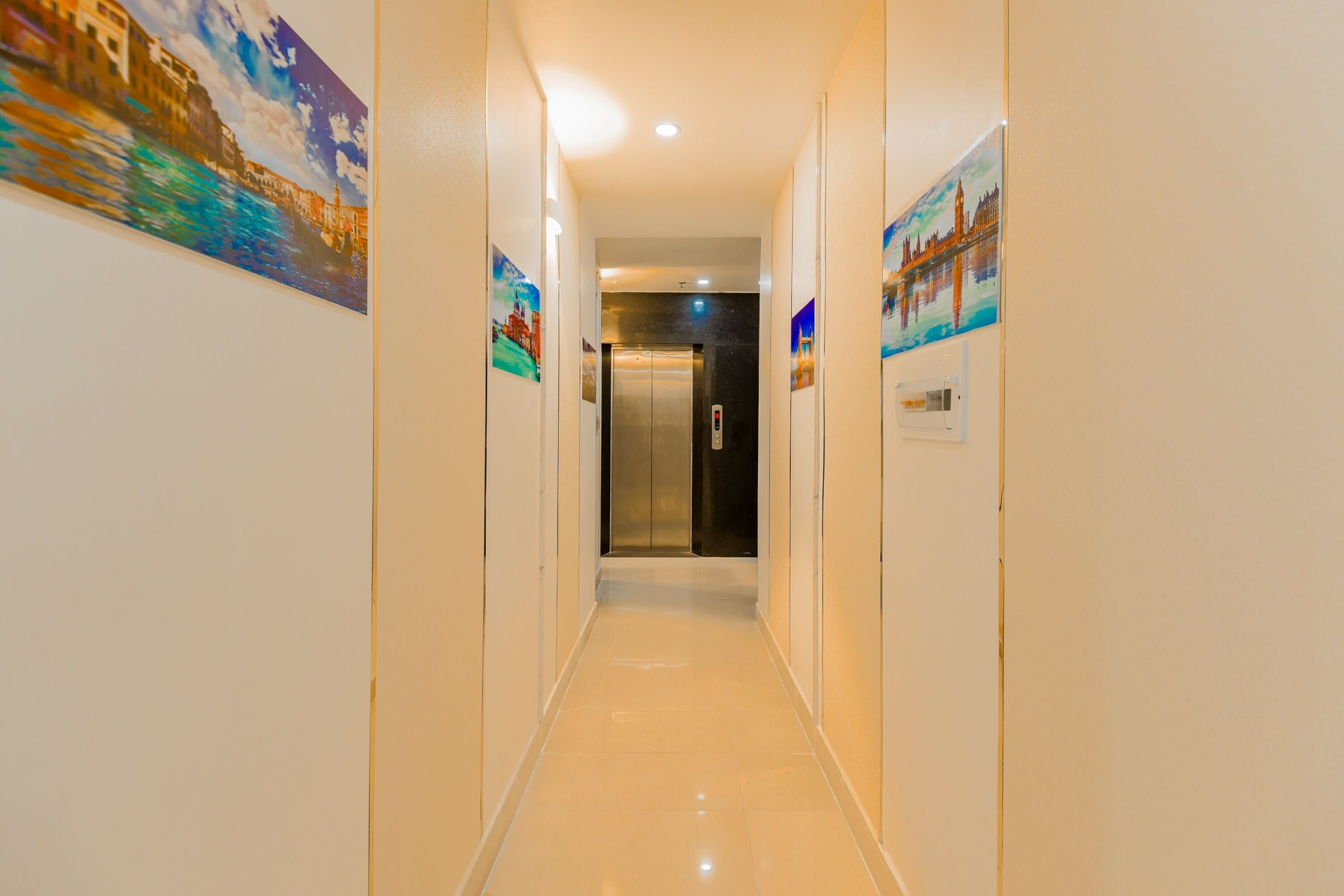 A hotel hallway with a shiny floor, an elevator, and artwork on the walls.