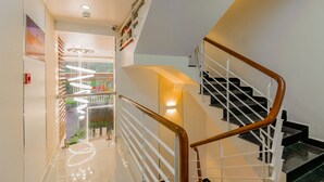 Un intérieur moderne avec un escalier, une balustrade en verre et une vue sur un jardin, visible à travers une porte vitrée.