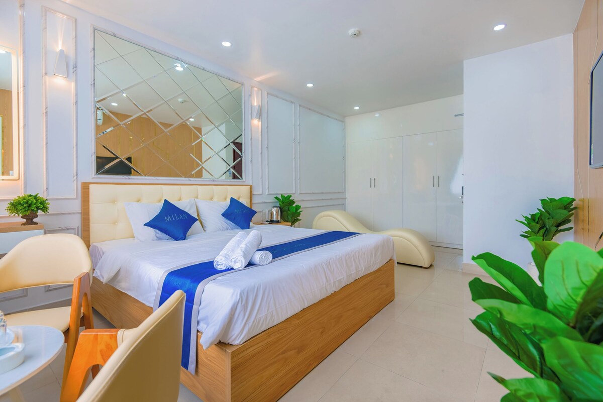 Ein modernes Hotelzimmer mit einem großen Bett, einem Schreibtisch und einem Stuhl. Es gibt ein großes Fenster mit Blick nach draußen.