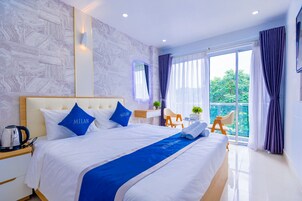 Quarto de hotel com uma cama grande, mesa de cabeceira, escrivaninha e varanda com cortinas.