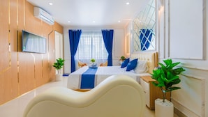 Une chambre moderne avec un lit aux lignes courbes, un téléviseur à écran plat, une grande fenêtre ornée de rideaux bleus et une plante en pot.