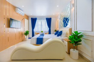 Quarto moderno com cama sinuosa, televisão de tela plana, janela ampla com cortinas azuis e um vaso de planta.