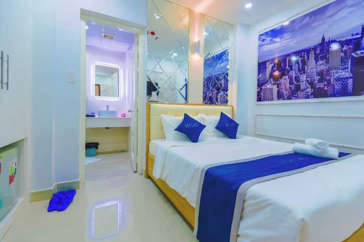 Une chambre d’hôtel avec un lit, une fresque représentant un paysage urbain, un miroir et une salle de bain équipée d’un lavabo et d’un miroir.