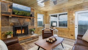 A cozy cabin interior with a stone fireplace, leather furniture, and a television mounted on the wall.