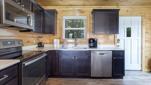 A modern kitchen with dark cabinets, stainless steel appliances, and a wooden ceiling.