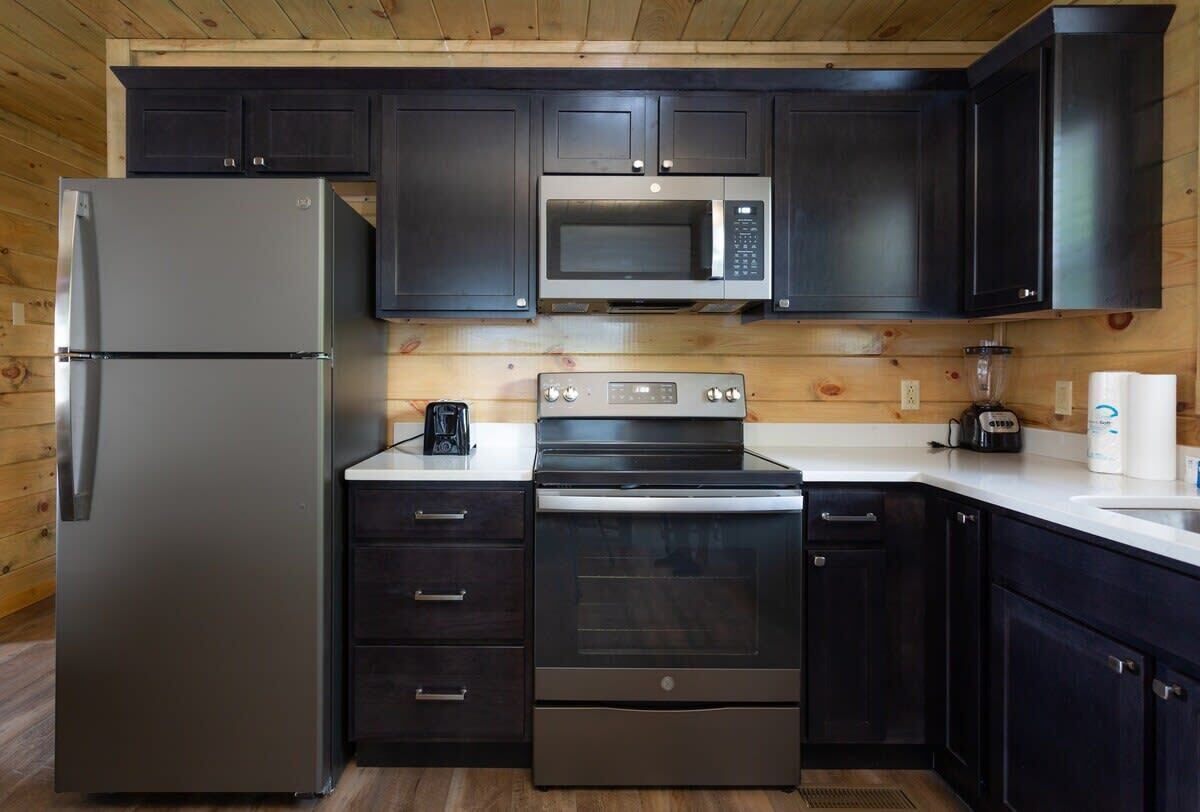 A compact kitchen with dark cabinets, a stainless steel refrigerator, a microwave, a stove, and a coffee maker.