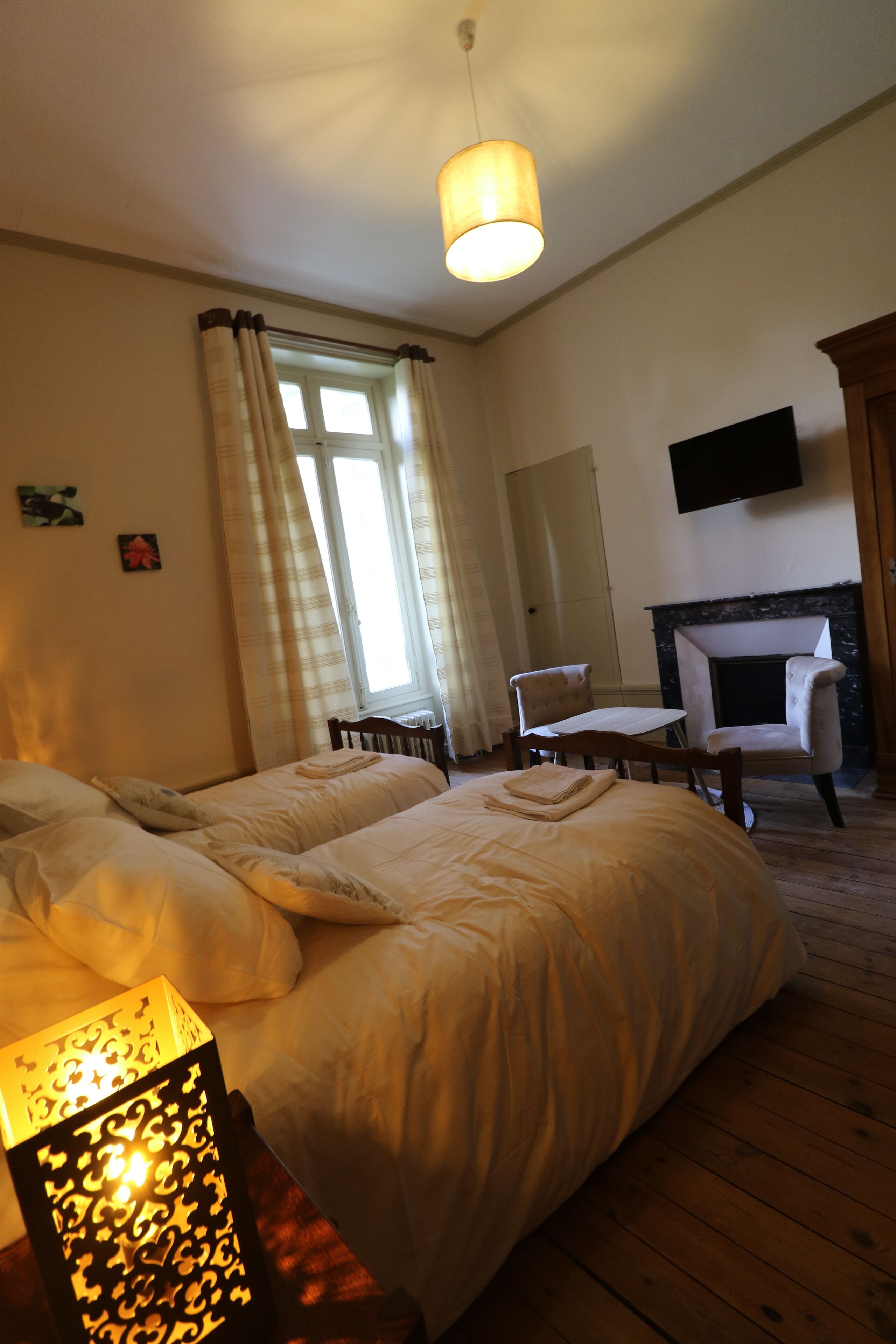 A bedroom with two beds, a wooden floor, a fireplace, a table, and a hanging TV.