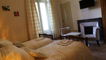 A bedroom with two beds, a wooden floor, a fireplace, a table, and a hanging TV.