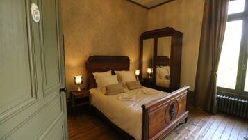 A bedroom with a wooden bed, a nightstand with a lamp, a large mirror, and a window with curtains.