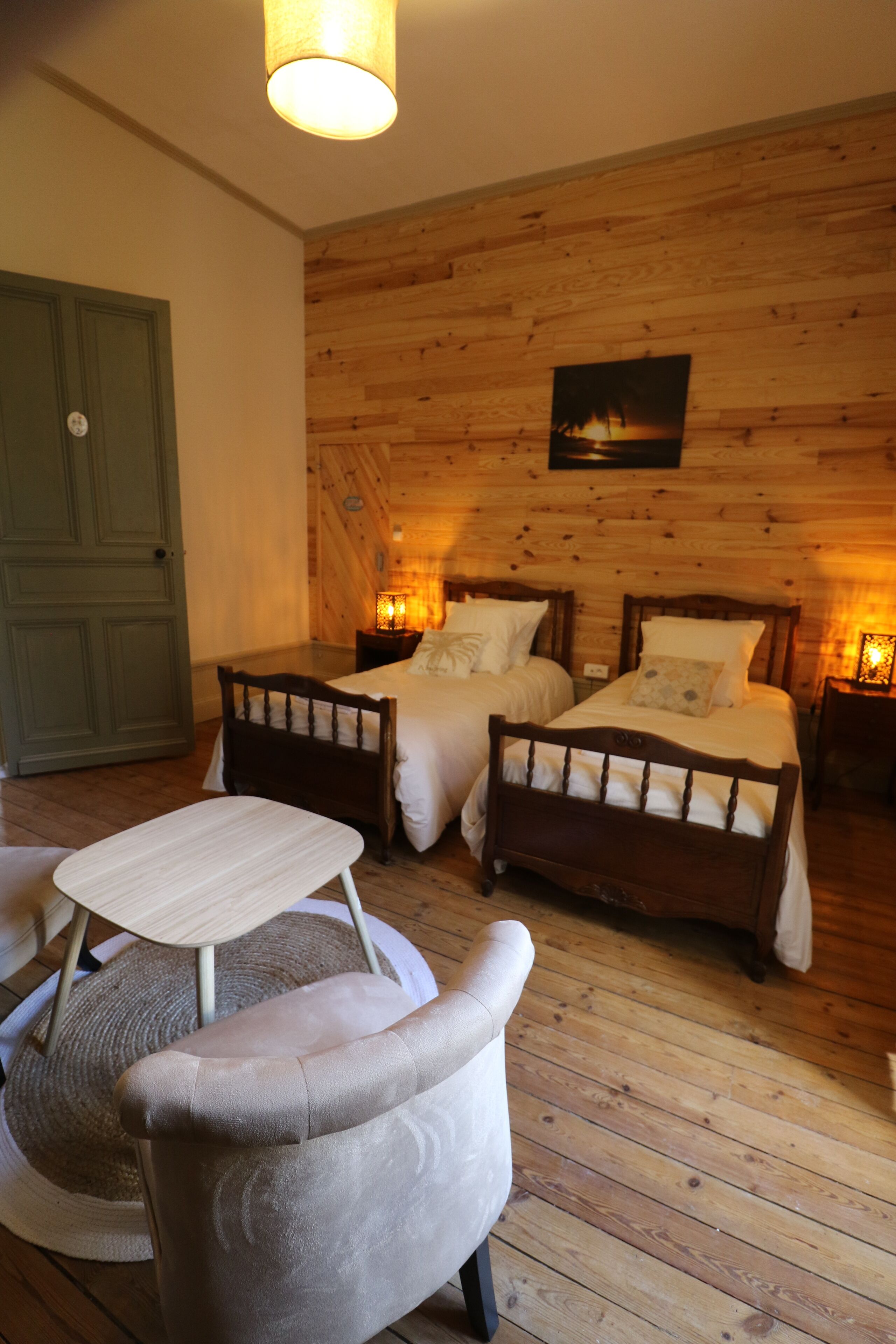 A wooden-paneled room with two beds, a small table, and a chair.