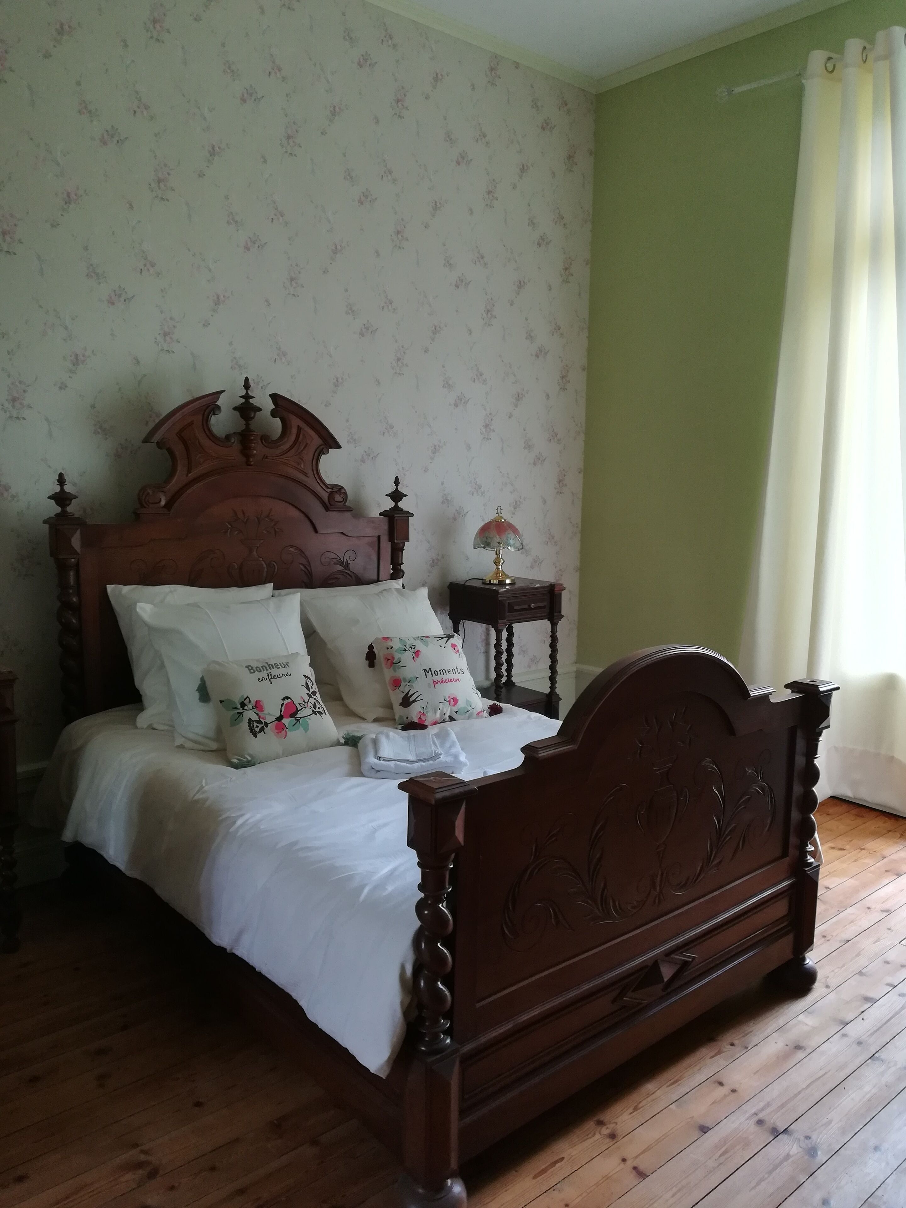 Een houten bed met een hoofdbord met bloemenprint, witte lakens en decoratieve kussens.