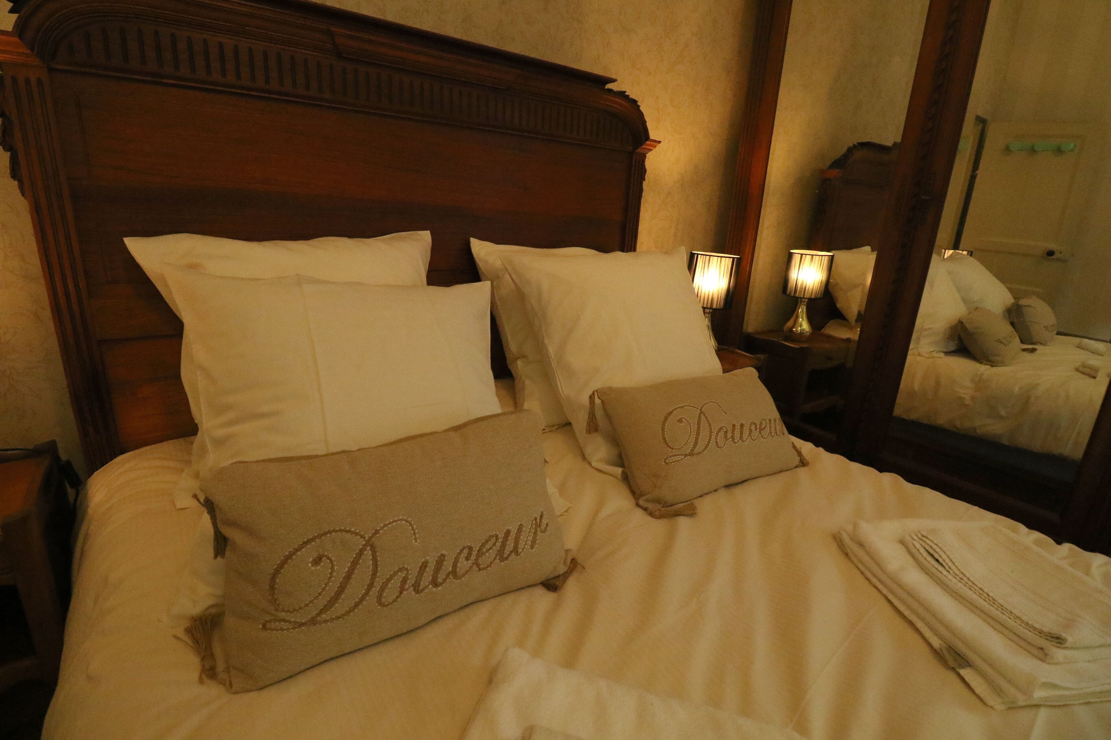 A neatly made bed with white linens and two decorative pillows with embroidered text.