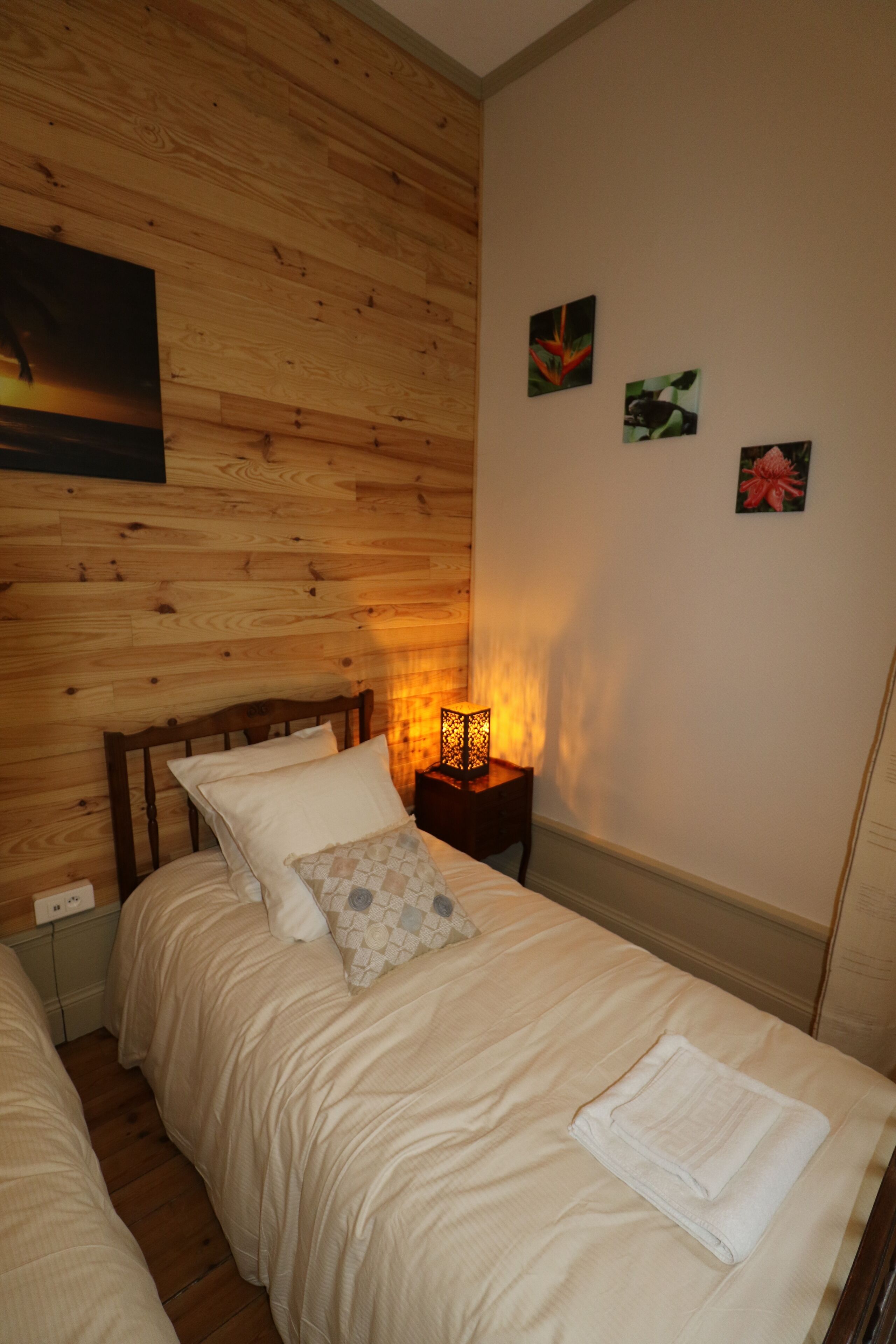 Un dormitorio con cabecera de madera, una mesita de noche con lámpara y una cama con toalla doblada.