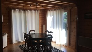 Een houten interieur met een ronde tafel en stoelen, een kamerbreed tapijt en gordijnen voor de ramen.