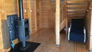 Een houten hut met een houtkachel, een ladder en een klein raam.