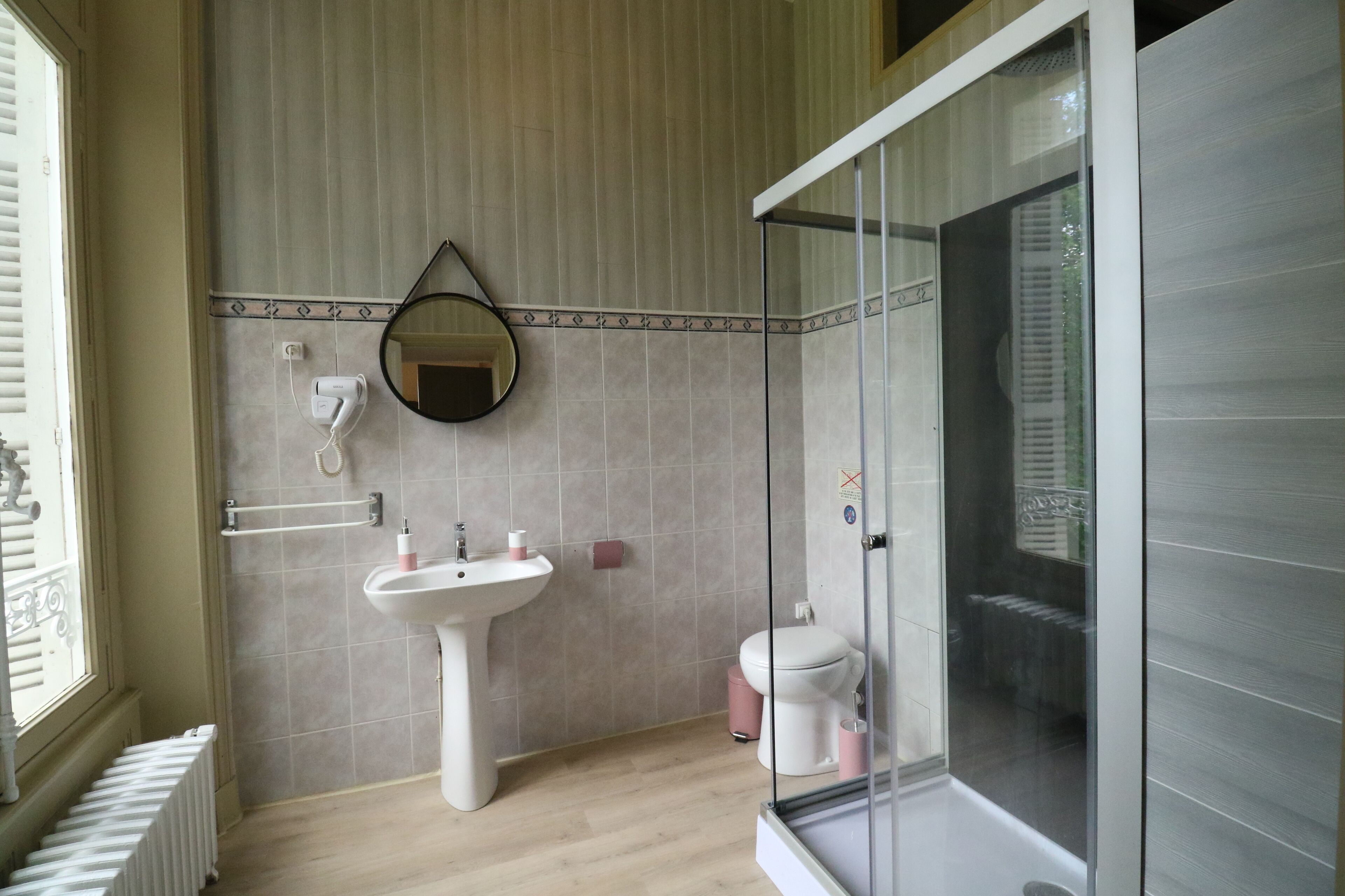 Un baño con un lavamanos pedestal, un inodoro, una ducha con mampara de vidrio y un espejo en la pared.
