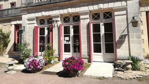 Un edificio histórico con fachada simétrica, ventanas grandes con contraventanas y una entrada central con un pequeño porche.
