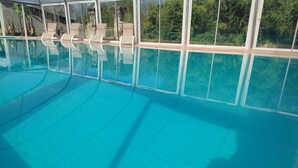 Una piscina azul cristalina con sillones de descanso y vistas a la vegetación a través de amplios ventanales.