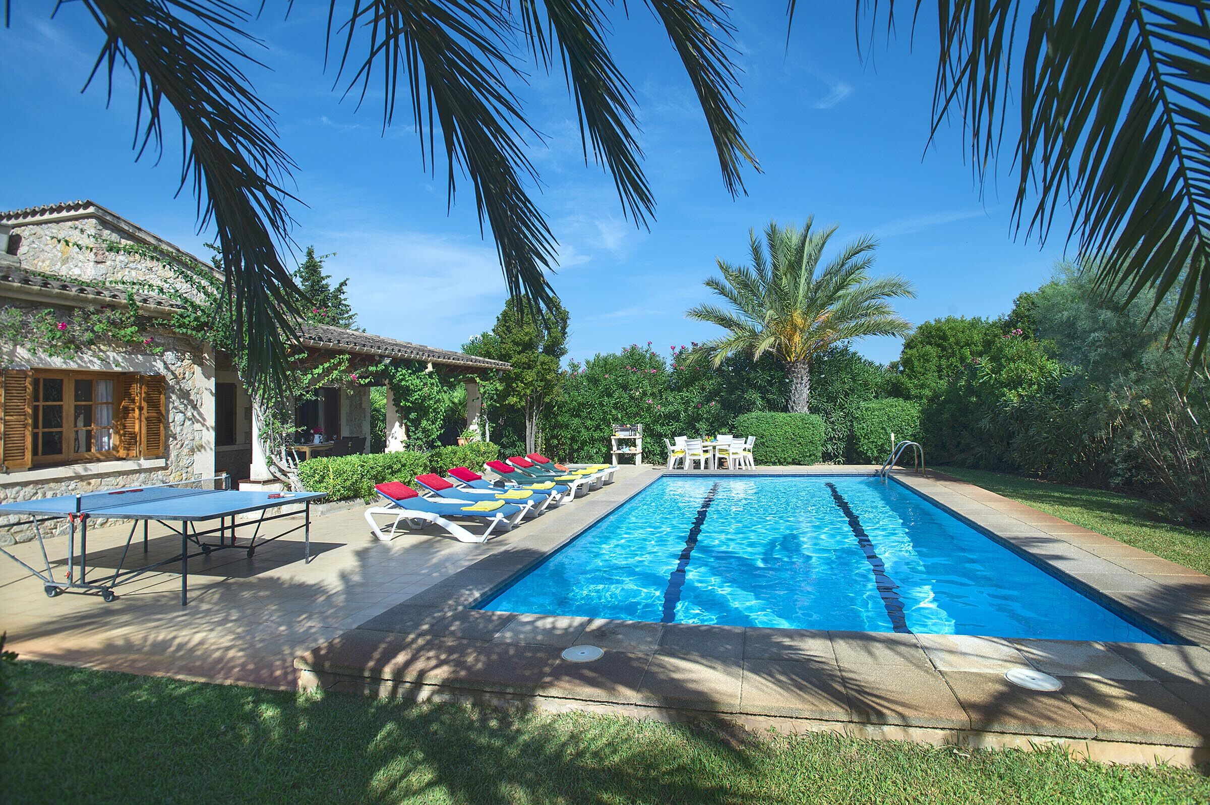 A swimming pool with lounge chairs and a table, surrounded by greenery and a stone building.