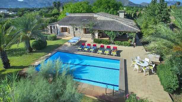 Un espace piscine agrémenté d ’un bâtiment en pierre, de chaises longues et offrant une vue sur les montagnes.