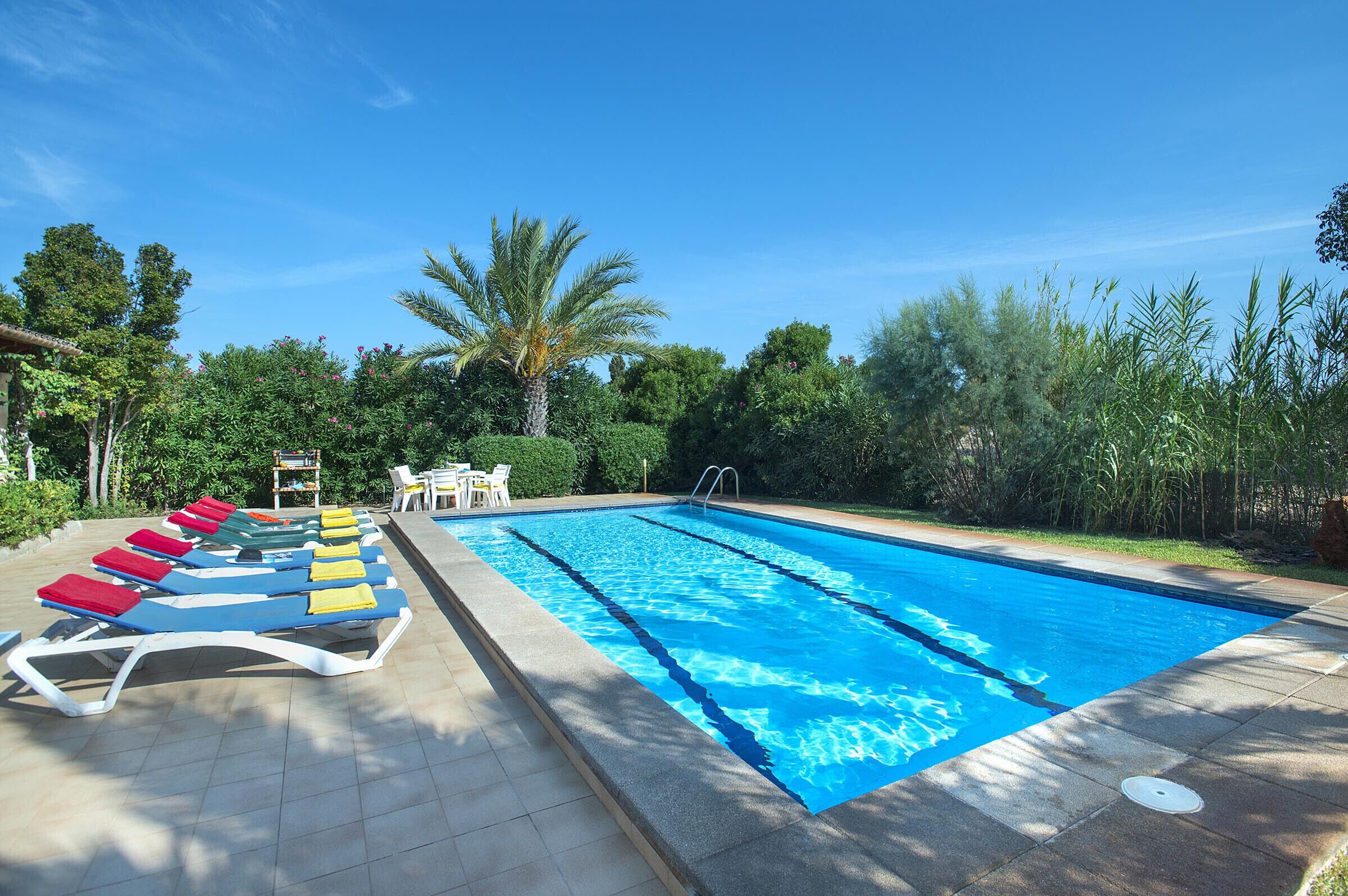 A swimming pool with lounge chairs and a small table, surrounded by greenery and trees.