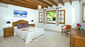 Une chambre avec un plafond en bois, un lit avec une literie blanche, une table de chevet avec une lampe, une fenêtre avec des rideaux et une vue sur la verdure à l’extérieur.