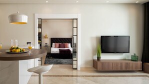 Een moderne woonkamer met een televisie, een eethoek met een tafel en stoelen, en een slaapkamer met een bed en nachtkastje.