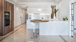 Een moderne keuken met een centraal eiland, barstoelen en een hanglamp.
