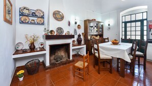 A dining area with a fireplace, wooden chairs, a table with a white tablecloth, and a cabinet with dishes. - Casa Da Aldeia (Alcaria Ruiva Mértola Beja)