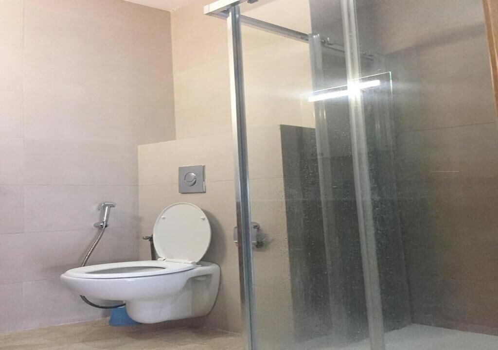 Ein Badezimmer mit Toilette, einer Duschkabine aus Glas und gefliesten Wänden.