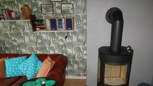 Uma sala de estar acolhedora com um sofá de couro marrom, uma mesinha preta com um jogo americano verde e uma lareira a lenha de madeira preta.
