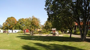 Um parque com parquinho, grama, árvores e um prédio ao fundo.