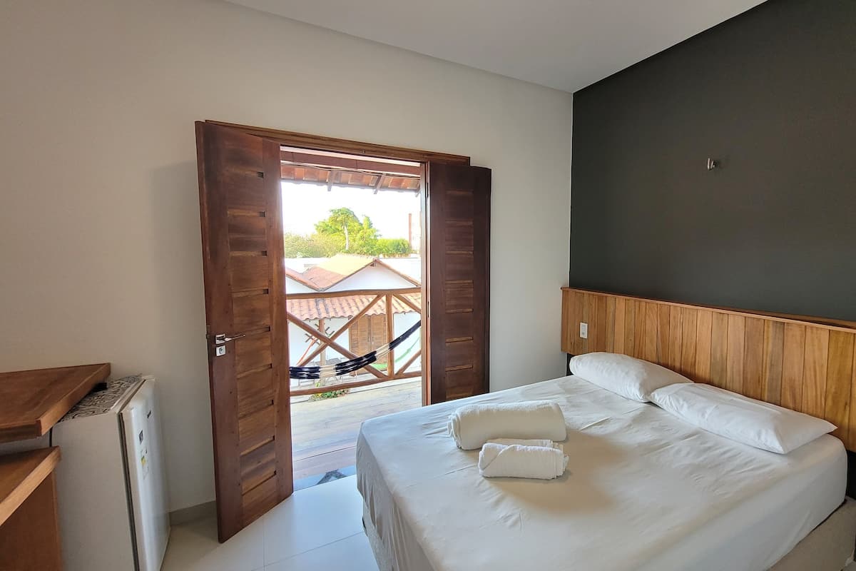 A bedroom with a bed, a wooden headboard, a white wall, and an open door leading to a balcony with a hammock.