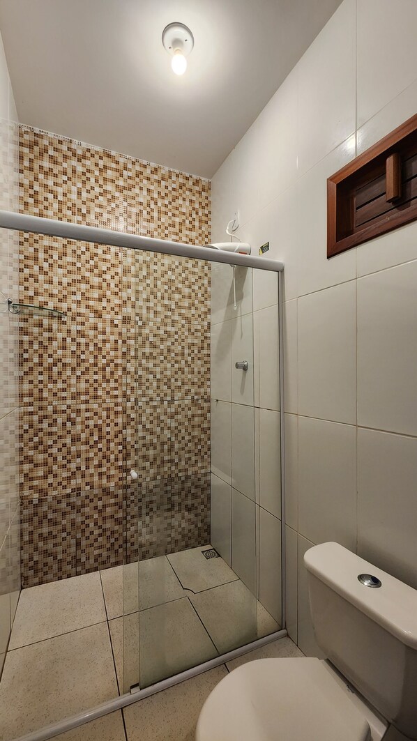Un baño moderno con pared de ducha de mosaicos, ducha con cerramiento de vidrio y un inodoro con estructura de madera.
