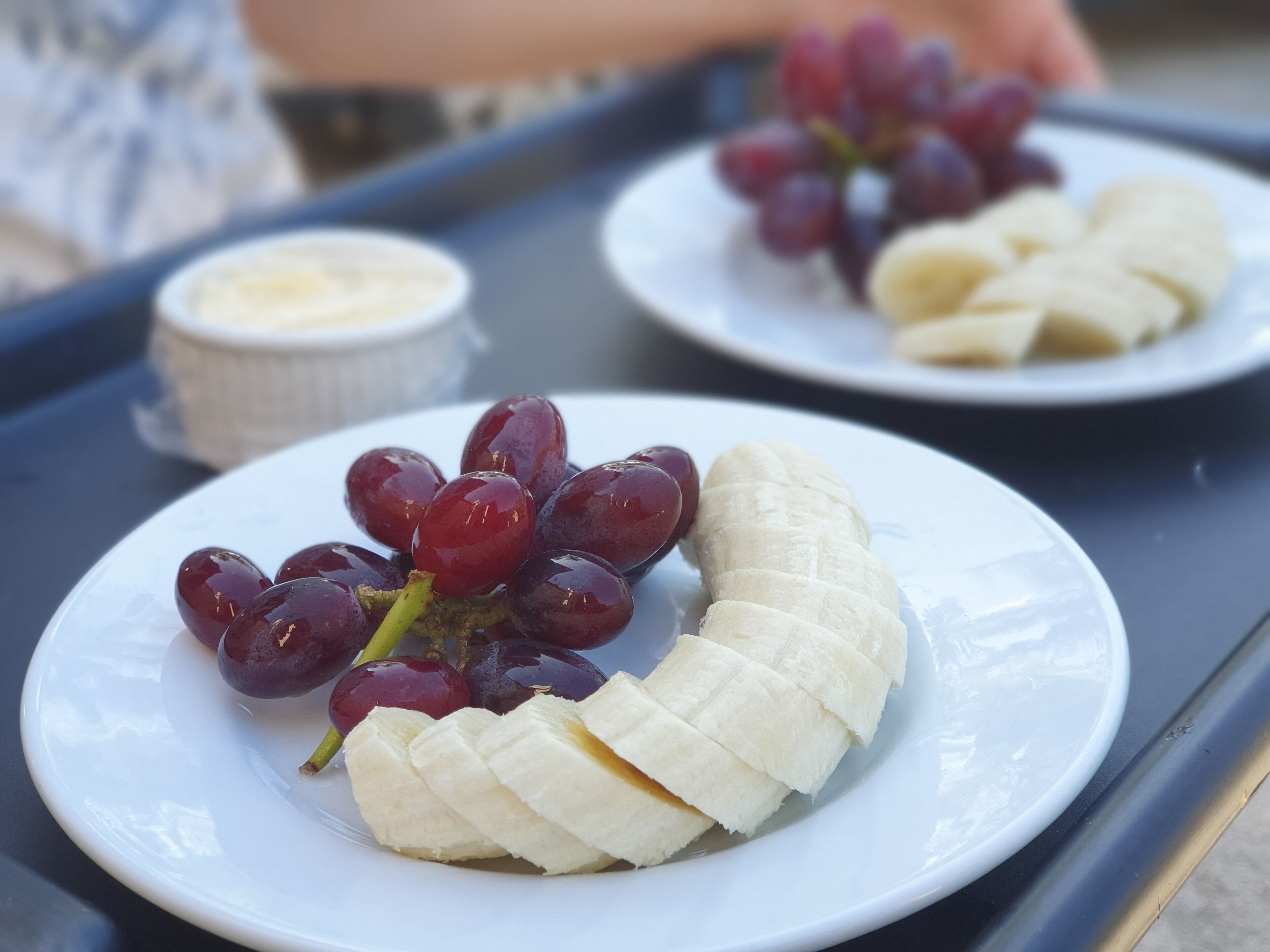 Dos platos blancos con rodajas de plátano y uvas sobre una bandeja.