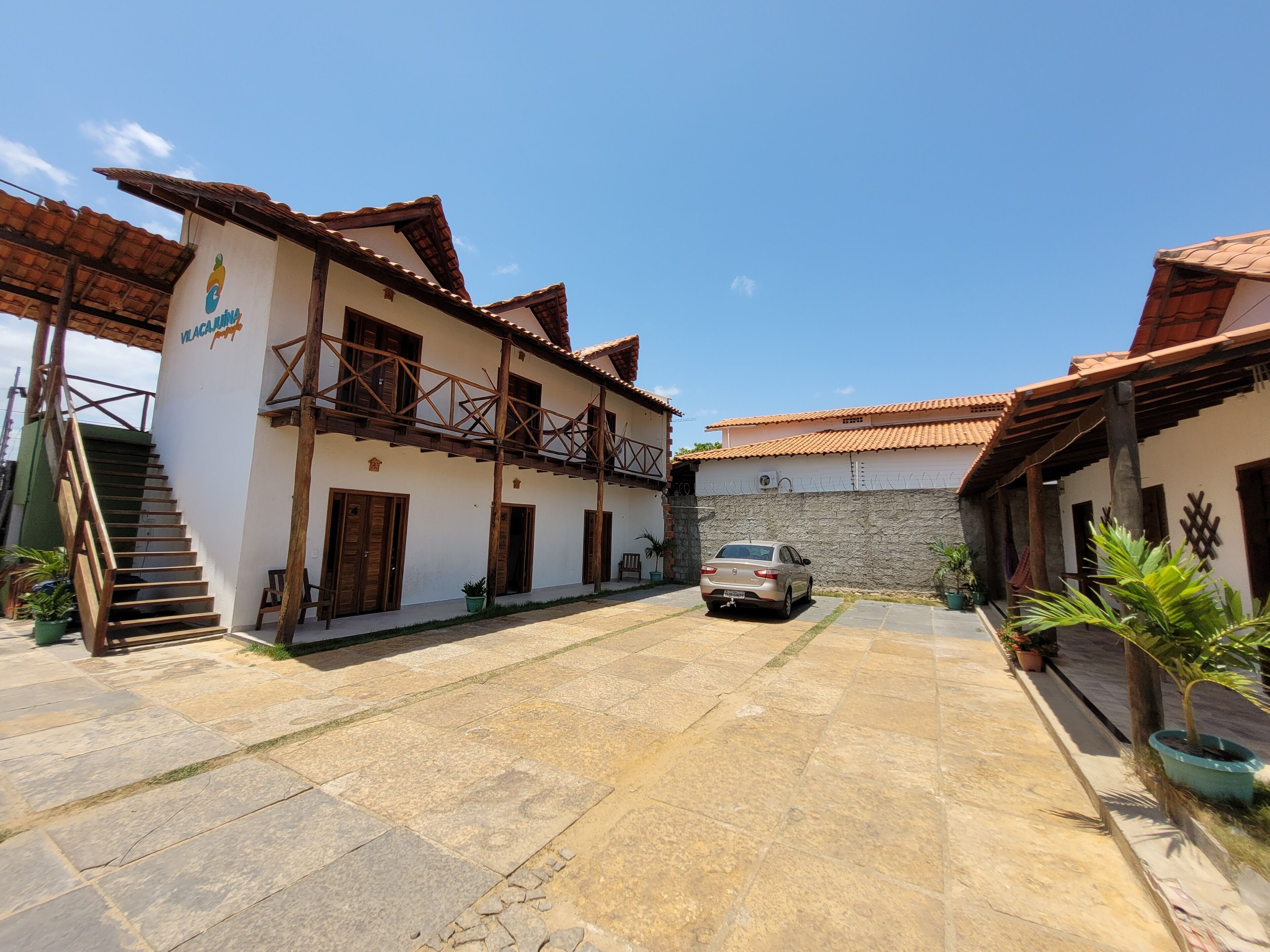 A courtyard with a car parked in front of a building with a tiled roof and a staircase leading to a wooden deck.