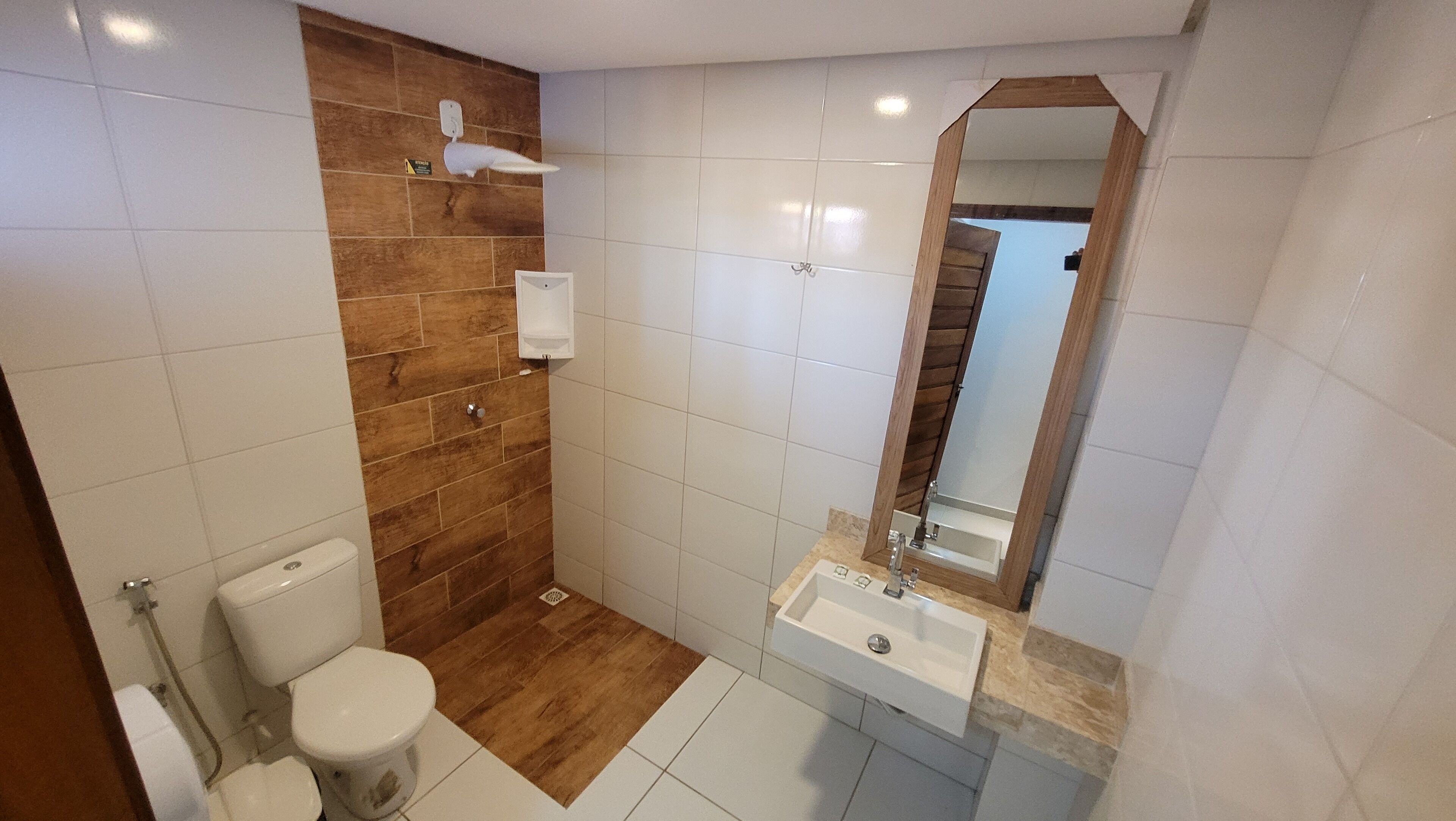 Un baño con inodoro, lavabo, espejo y pared de acento de madera.