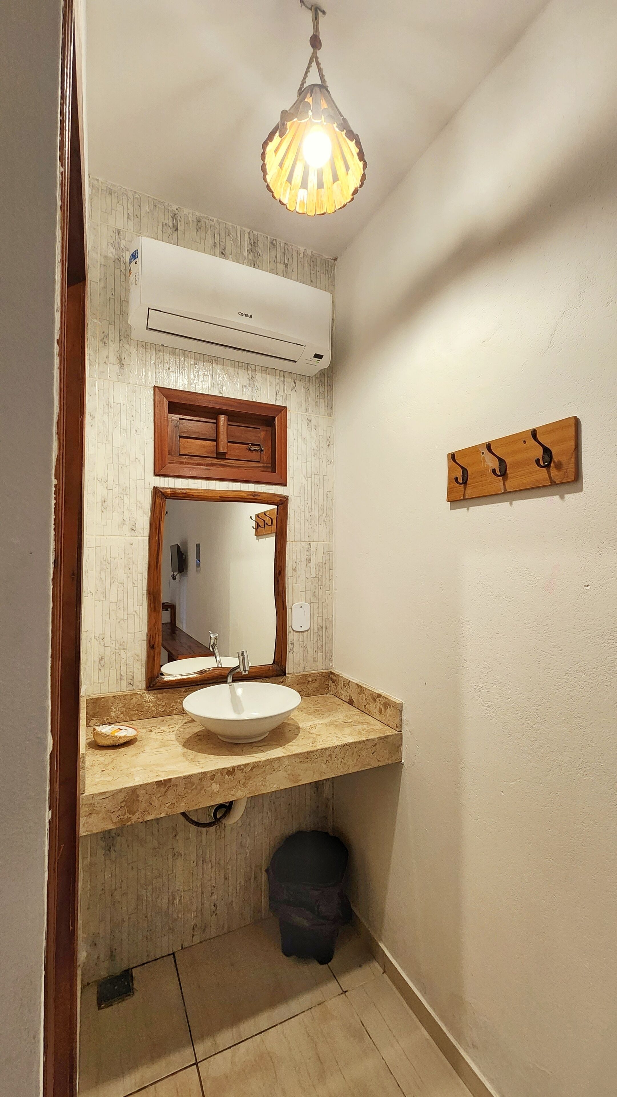 A bathroom with a white sink, wooden cabinet, and a mirror above it. There is a hanging light fixture and a wall-mounted towel rack.