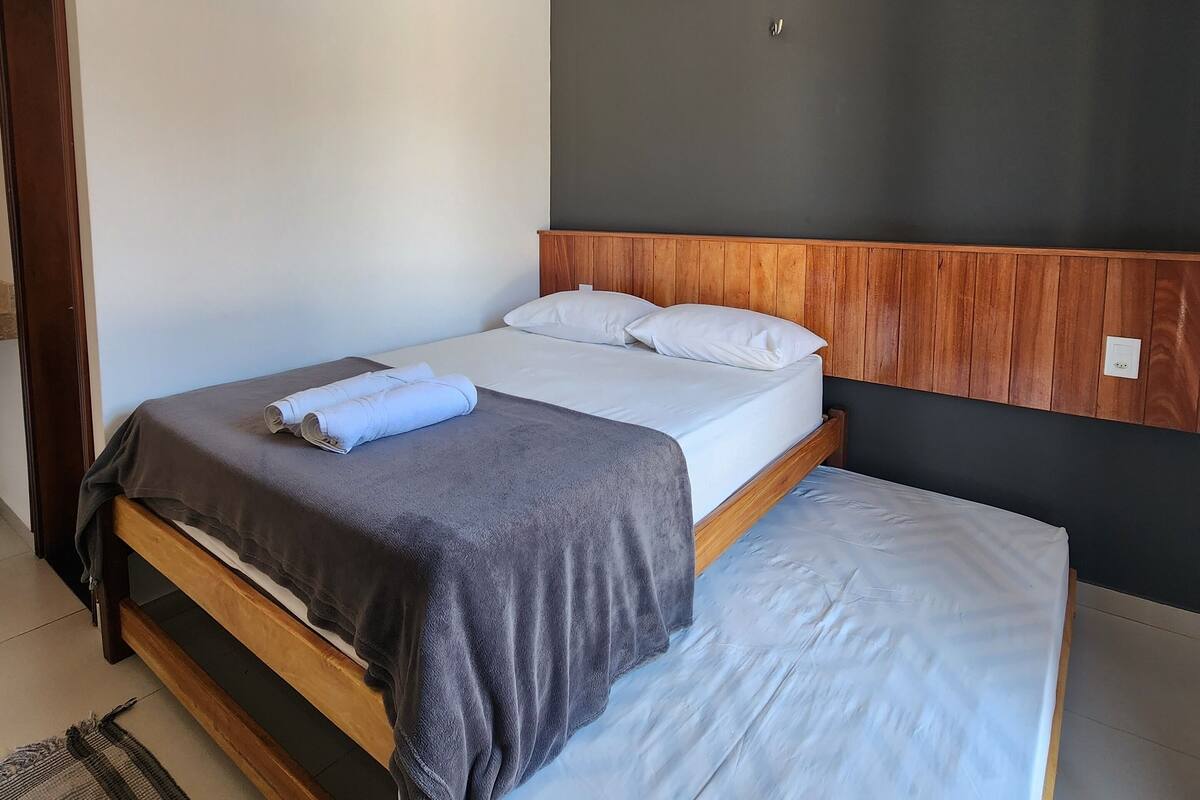 A double bed with a wooden headboard, a grey blanket, and a blue towel.