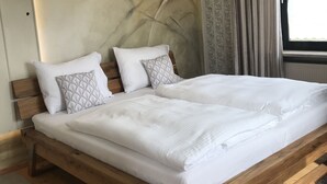 A bedroom with a wooden bed frame, white bedding, and a large window with curtains. - Holiday home with sauna and garden lounge (Lauingen)