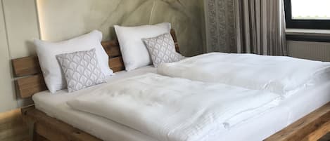 A bedroom with a wooden bed frame, white bedding, and a large window with curtains.