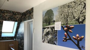 A hallway with a wooden railing, a door, and a wall with floral wallpaper and a framed picture of trees. - Holiday home with sauna and garden lounge (Lauingen)