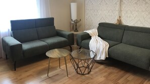 A living room with two green sofas, a glass coffee table, a wall clock, and a chandelier. - Holiday home with sauna and garden lounge (Lauingen)