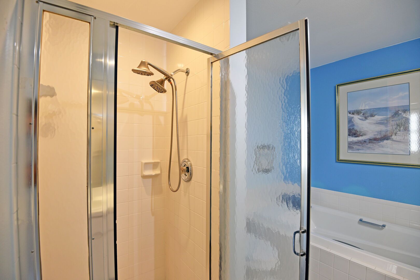 A glass-enclosed shower with a handheld showerhead and a wall-mounted control panel.