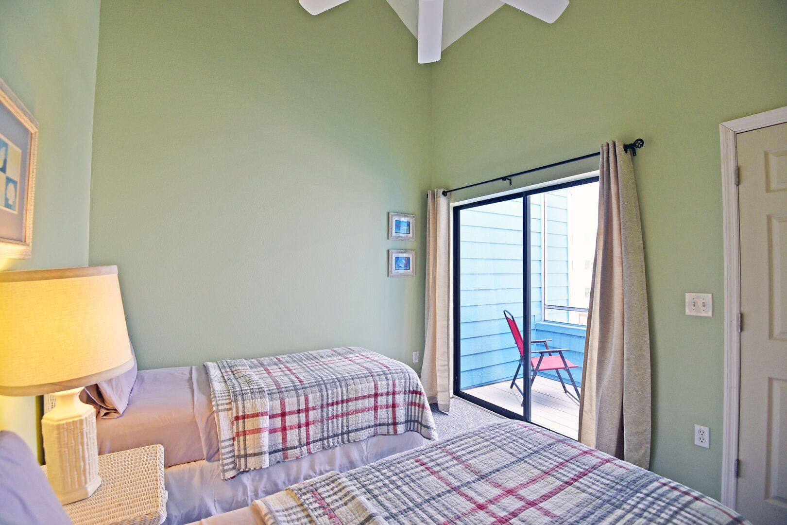Une chambre avec deux lits, une fenêtre avec des rideaux, une lampe et une vue sur le balcon extérieur.