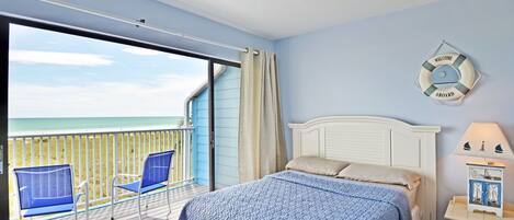 A bedroom with a large window, a bed with a blue quilt, two blue chairs, and a "Welcome Aboard" sign.