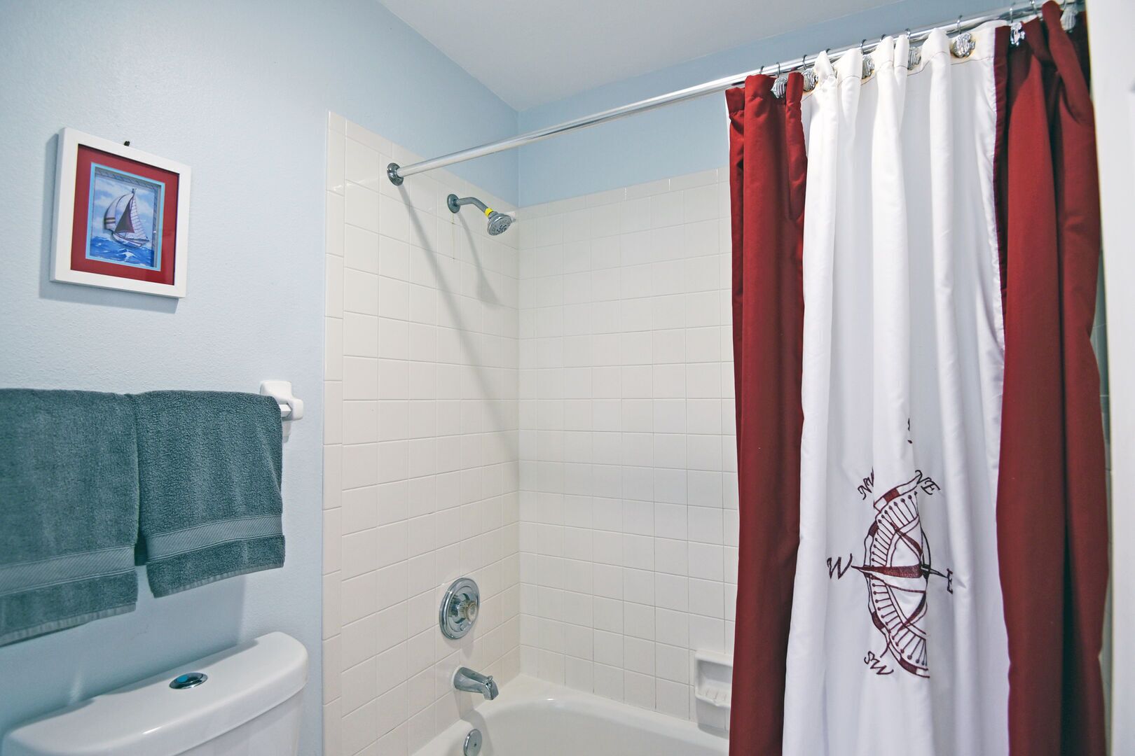 Une salle de bain avec une baignoire, une douche et des toilettes. On y trouve un porte-serviettes avec des serviettes et un tableau encadré accroché au mur.