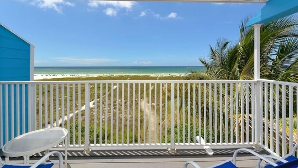Un balcon donnant sur la plage, avec des balustrades blanches et deux fauteuils de jardin bleus.