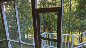 Eine Holzterrasse mit weißer Geländer, die auf einen bewaldeten Bereich blickt.