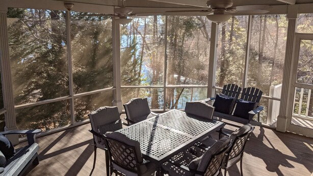 Eine überdachte Terrasse im Freien mit Tisch und Stühlen, großen Fenstern und einem Deckenventilator.